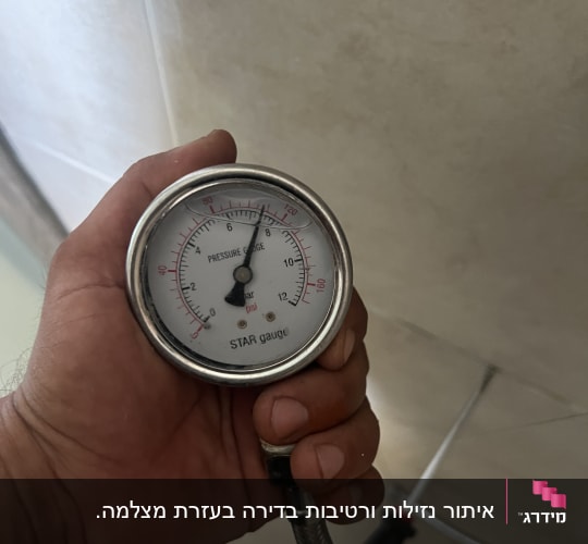 מד לחץ מים מוחזק ביד ליד צינור מתכת